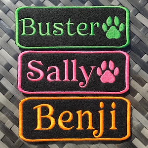 Może przedstawiać: Trzy prostokątne naszywki z haftowanymi imionami i odciskami łap. "Buster" jest w kolorze zielonym z zielonym odciskiem łapy, "Sally" jest w kolorze różowym z różowym odciskiem łapy, a "Benji" jest w kolorze pomarańczowym. Wszystkie imiona są na czarnej tkaninie.