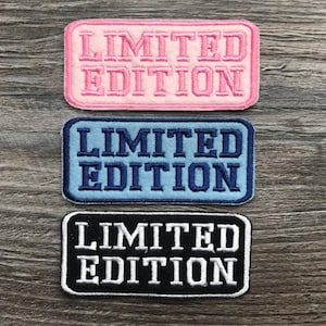 May include: Three embroidered patches with the text "Limited Edition" in different colours. The top patch is pink with white text, the middle patch is blue with white text, and the bottom patch is black with white text.