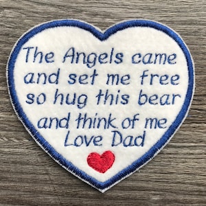 Può includere: Toppa a forma di cuore in feltro bianco con cuciture blu intorno ai bordi. La toppa ha un testo ricamato in blu che recita "The Angels came and set me free so hug this bear and think of me, Love Dad". Un piccolo cuore in feltro rosso è ricamato al centro inferiore della toppa.