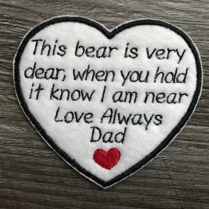 May include: White heart-shaped felt patch with black embroidered text that reads "This bear is very dear, when you hold it know I am near Love Always Dad" and a small red felt heart.