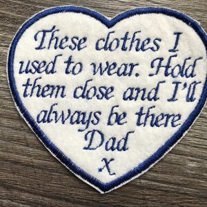 May include: A heart-shaped white fabric patch with a dark blue embroidered border and dark blue stitched text that reads: These clothes I used to wear. Hold them close and I'll always be there Dad x. The patch features a clean, stitched edge finish.