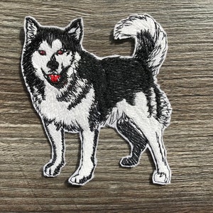 Puede incluir: Parche bordado de un perro husky blanco y negro con la lengua roja. El perro está de pie con la cabeza girada hacia la izquierda y la cola enroscada.