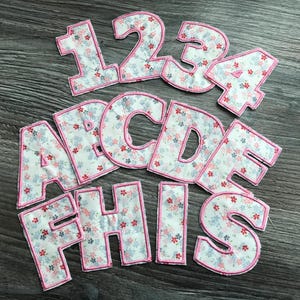 May include: A set of pink and white fabric letters and numbers with a floral pattern. The letters spell out "THIS" and the numbers are 1, 2, 3, and 4.
