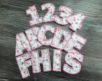 May include: A set of pink and white fabric letters and numbers with a floral pattern. The letters spell out "THIS" and the numbers are 1, 2, 3, and 4.