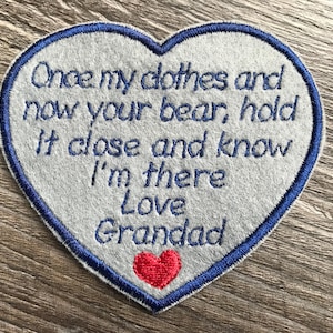 May include: A heart-shaped fabric patch with a light gray base and a dark blue embroidered border. The text reads: Once my clothes and now your bear, hold it close and know I'm there Love Grandad. A small red embroidered heart sits below the text.
