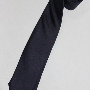 May include: A navy blue tie with a repeating pattern of small red dots. The tie is rolled up at the top, with the rest of the tie lying flat. The tie is made of a smooth fabric.