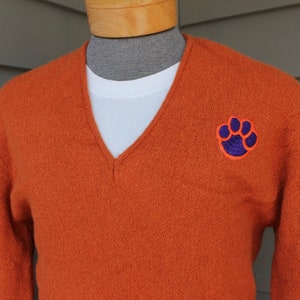 May include: Orange v-neck sweater with a purple paw print embroidered on the right side.