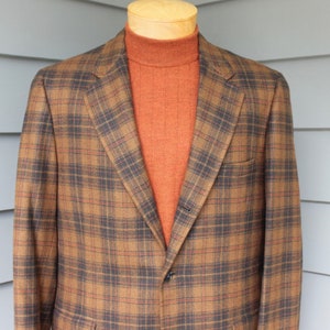 May include: A brown and black plaid blazer with a single button closure. The blazer is worn over a rust-colored turtleneck sweater.