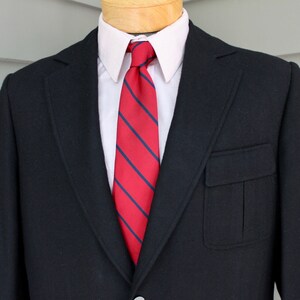 May include: A black blazer with a single button closure and a red and navy striped tie. The blazer has a flap pocket on the left side.