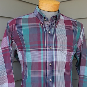 May include: A long-sleeved button-down shirt with a plaid pattern in shades of burgundy, teal, white, and navy blue.