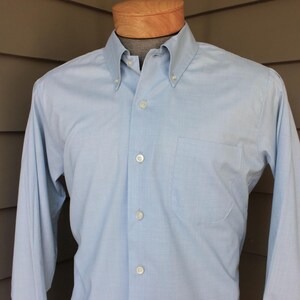 May include: A light blue long-sleeved button-down shirt with a single chest pocket.