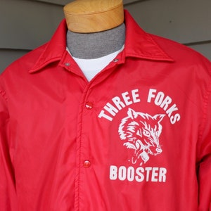 May include: Red nylon jacket with a white wolf graphic and the text "Three Forks Booster" on the front.