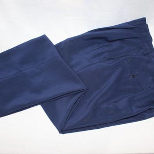 May include: A pair of dark blue pleated pants. The pants are folded in half and laid flat on a white surface.