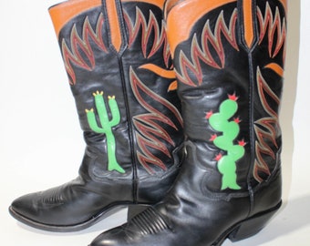 Könnte beinhalten: Ein Paar schwarze Leder-Cowbo Stiefel mit braunen Lederoberteilen. Die Stiefel haben ein Flammenmuster und ein Kaktusdesign an der Seite.