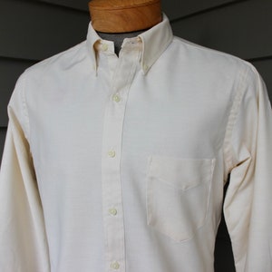 May include: A long-sleeved, button-down shirt in a creamy white color. The shirt has a single chest pocket and a classic collar.