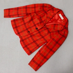 May include: A double-breasted blazer in a vibrant orange plaid pattern with black and brown accents. The jacket features a classic collar, two rows of black buttons, and long sleeves. The interior lining is a solid red.