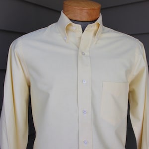 May include: A pale yellow long-sleeved button-down shirt with a single pocket on the left side.