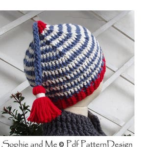 May include: A blue and white striped crocheted hat with a red tassel. The hat has a long tail that hangs down the back of the neck. The hat is on a mannequin head.