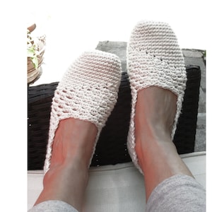 May include: A pair of crocheted white slippers with a lacy design. The slippers are worn by a person sitting on a wicker chair. The image includes the text "Sophie and Me © Pdf Pattern Design".