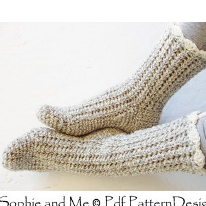 Peut inclure: Une paire de chaussettes au crochet de couleur beige clair avec une bordure blanche au crochet. Les chaussettes sont faites avec un point texturé et sont posées sur une surface blanche.