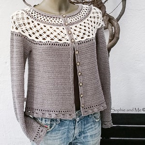 May include: A crocheted cardigan with a white crocheted trim around the neckline and hem. The cardigan is a light brown color and has a button closure.
