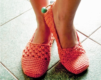 May include: A pair of orange crocheted slippers with a green bead accent. The slippers are worn on a tiled floor.