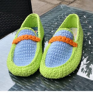 Puede incluir: Un par de mocasines de crochet en verde, azul y naranja. Los mocasines tienen un ribete contrastante y una correa decorativa.