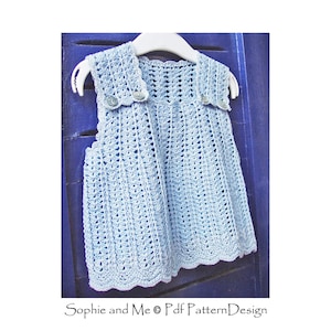 May include: A light blue crocheted baby dress with a scalloped hem and button closures. The dress is hanging on a hanger against a blue wooden background.