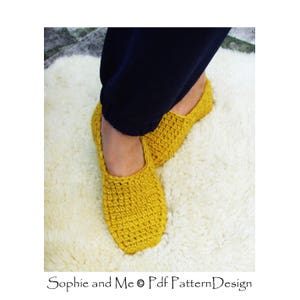 May include: A pair of yellow crocheted slippers on a white fluffy rug. The slippers are made with a simple stitch pattern and have a rounded toe.