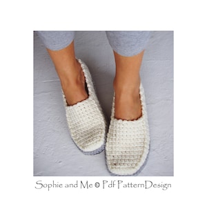 May include: A pair of white crocheted slippers with gray soles. The slippers are worn by a person standing on a gray surface. The text "Sophie and Me &copy; Pdf PatternDesign" is visible at the bottom of the image.