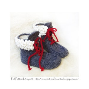 Può includere: Un paio di stivaletti grigi lavorati a mano a maglia con finiture bianche soffici e lacci rossi. Queste accoglienti pantofole a tema invernale sono perfette per l'uso in casa. Gli stivaletti sono esposti su una superficie bianca e morbida.