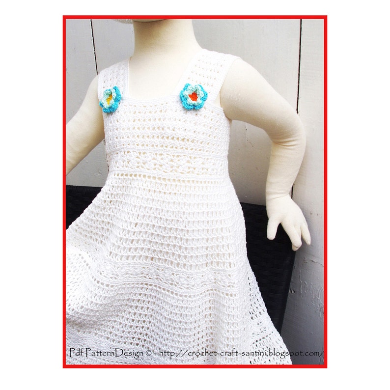 May include: White crochet dress with a sleeveless design and a scalloped hem. The dress has two small crocheted flowers on the bodice, one blue and one yellow.