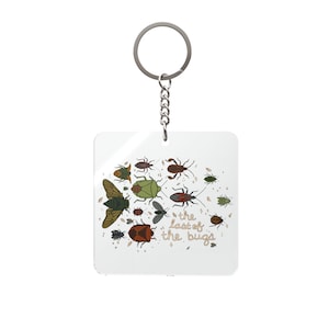 Op de afbeelding: Een witte vierkante sleutelhanger met een verzameling geïllustreerde insecten in verschillende kleuren. De sleutelhanger heeft een zilveren ring en ketting. De tekst "the last of the bugs" is geschreven in een speels lettertype.