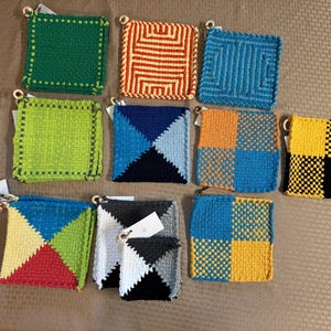 Könnte beinhalten: Eine Sammlung von zehn quadratischen, handgehäkelten Topflappen in verschiedenen Farben und geometrischen Mustern, darunter einfarbiges Grün, orangefarbene und blaue Labyrinth-Muster, Limettengrün, blaue und schwarze Dreiecke sowie Karomuster.