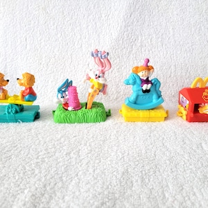 May include: A collection of vintage McDonald's Happy Meal toys. The toys include figures of cartoon characters on a seesaw, in a garden, on a rocking horse, and a McDonald's restaurant.