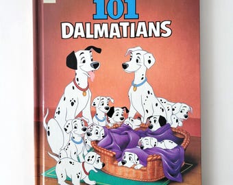 Peut inclure: Un livre cartonné intitulé "Disney's 101 Dalmatians" avec des illustrations de chiens dalmatiens. La couverture montre des dalmatiens adultes et chiots, avec le titre en grandes lettres bleues et blanches.