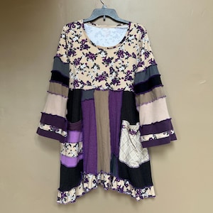 May include: A patchwork tunic with a floral print top, purple, brown, and black stripes, and a ruffled hem.