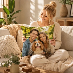May include: A square throw pillow featuring a printed photograph of a man, a woman, and a brown and white spaniel dog sitting together in a sunlit park with green trees in the background. The pillow has a smooth fabric surface and edges.