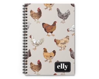 May include: Spiral-bound notebook featuring a repeating pattern of illustrated chickens in various colors on a light gray background. The notebook has a black label with the name "elly" in white text.
