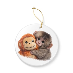 May include: A round ceramic ornament featuring a brown and orange plush monkey hugging a gray monkey. The ornament has a gold string for hanging. The design is printed on a white background.