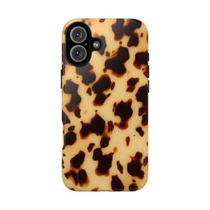 Puede incluir: Una funda rectangular para smartphone con un patrón clásico de carey con manchas irregulares de color marrón oscuro y negro sobre un fondo translúcido de color ámbar y crema. La funda incluye un recorte circular para una cámara doble.