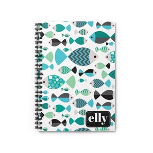 May include: Spiral-bound notebook with a white cover featuring a pattern of teal, turquoise, black, and gray fish. The word "elly" is printed on a black label in the lower right corner. The notebook's pages are held together by a black spiral binding.