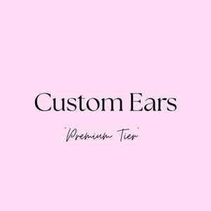 Peut inclure: Fond rose avec les mots "Custom Ears" en gras, en noir. En dessous, en écriture cursive, les mots "Premium Tier" sont affichés.