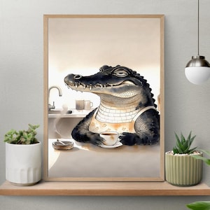 May include: Watercolor art print of an alligator wearing an apron and holding a cup of coffee. The alligator is in a kitchen setting, with a sink and plants in the background. The artwork is framed in a light brown wooden frame.