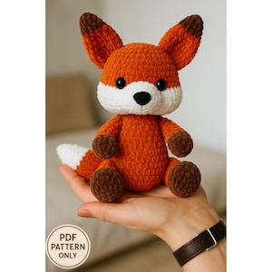 May include: A crocheted fox plushie in shades of orange, white, and brown. The fox has large ears, a white muzzle, and a fluffy tail. The text "PDF PATTERN ONLY" is in a white circle in the lower left corner.