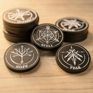 May include: Black, circular tokens with white symbols and text, arranged on a light wooden surface. The tokens feature designs and the words "HOPE", "SPELL", and "FEAR". Some tokens are stacked.