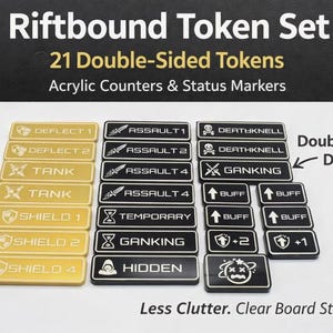 May include: A set of 21 double-sided acrylic tokens for Riftbound, with various status markers. The tokens are rectangular, with gold and black color schemes. Text on the tokens includes "DEFLECT", "ASSAULT", "TANK", "SHIELD", and "BUFF".