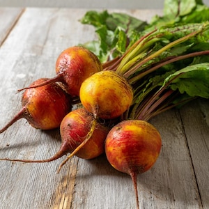 May include: A cluster of golden beets with red and yellow hues, featuring long, slender roots and vibrant green leaves. The beets are arranged on a weathered wooden surface, showcasing their fresh, natural appearance.