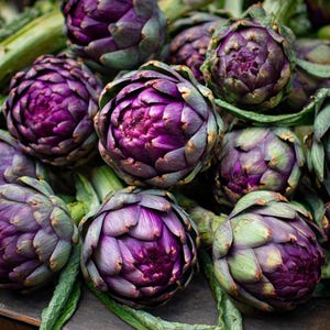 May include: A close-up shot of several purple artichokes. The artichokes have layered, textured leaves with a deep purple hue at the center, transitioning to green at the tips. The image showcases the fresh produce, highlighting their vibrant colors and intricate details.