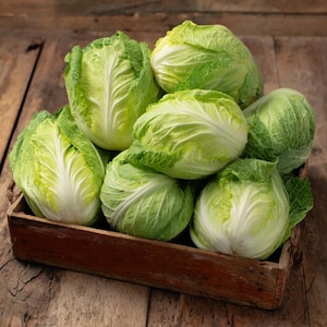 May include: A wooden crate filled with fresh, green cabbages. The cabbages have tightly packed, pale green leaves with a white core. The crate sits on a rustic wooden surface, creating a natural and wholesome aesthetic.